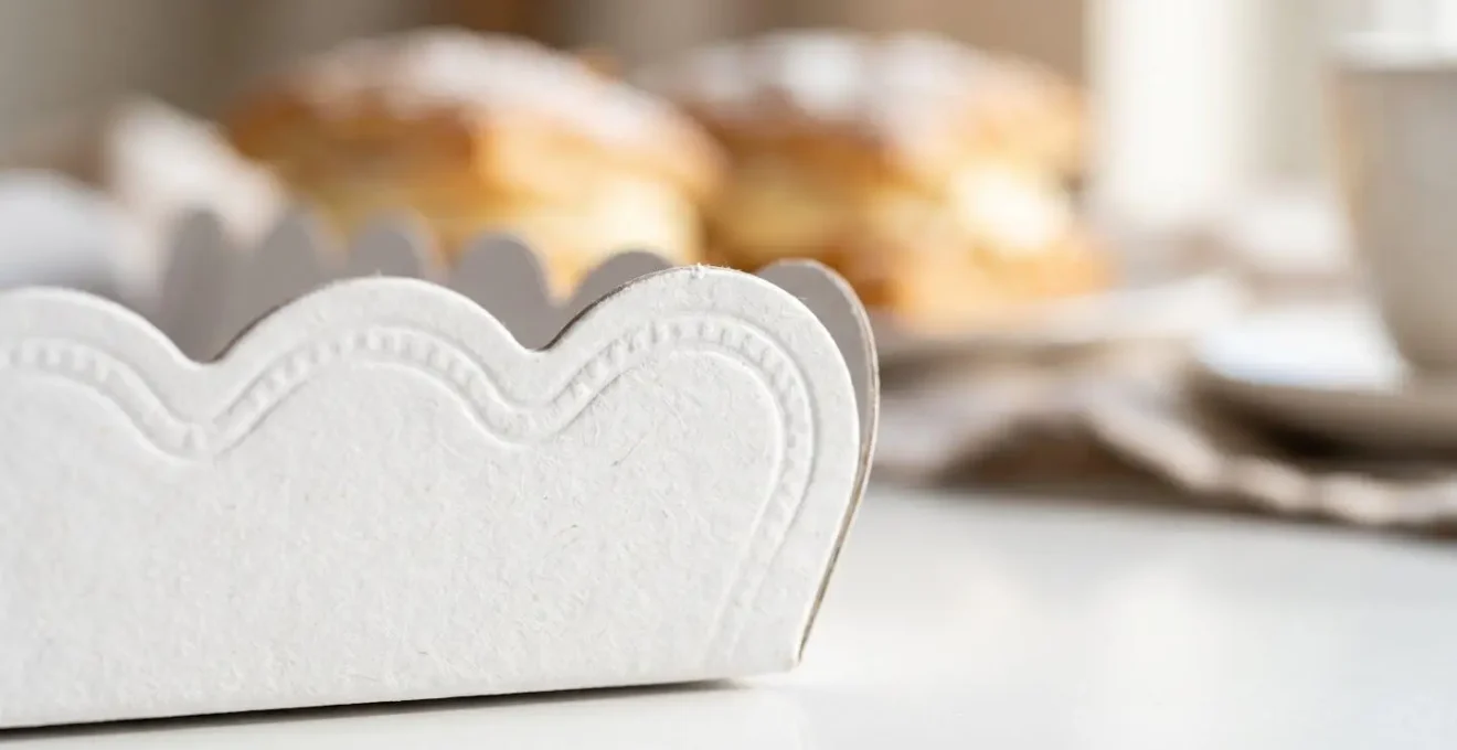 Gros plan sur le bord festonné d'un plateau en carton blanc avec la texture du papier visible et une pâtisserie floue en arrière-plan